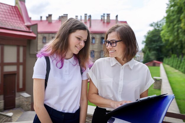 Ritratto all'aperto di insegnante femminile e studentessa parlante. Campus, sfondo dell'edificio scolastico, ritorno al college, ritorno a scuola, inizio delle lezioni