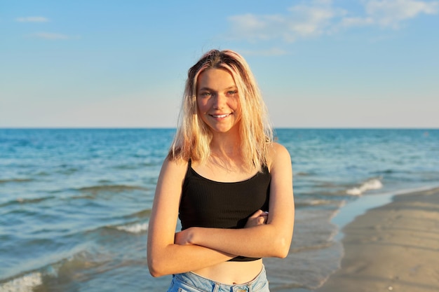Ritratto all'aperto di un'adolescente femmina di 16 anni Bella donna sorridente guardando la fotocamera con i capelli bagnati sulla spiaggia sabbiosa del mare nella luce del tramonto