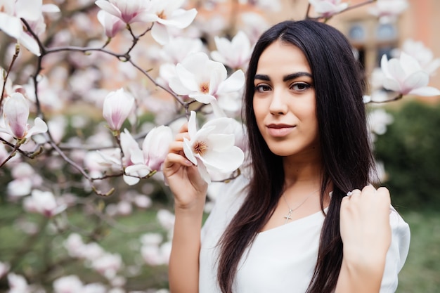 Ritratto all'aperto di una giovane bella donna vicino all'albero di magnolia con i fiori.