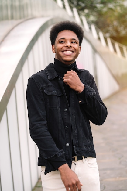 Ritratto alla moda di un bell'uomo marocchino con capelli afro che tocca la giacca con vestiti in stile urbano e molto sorridente e felice