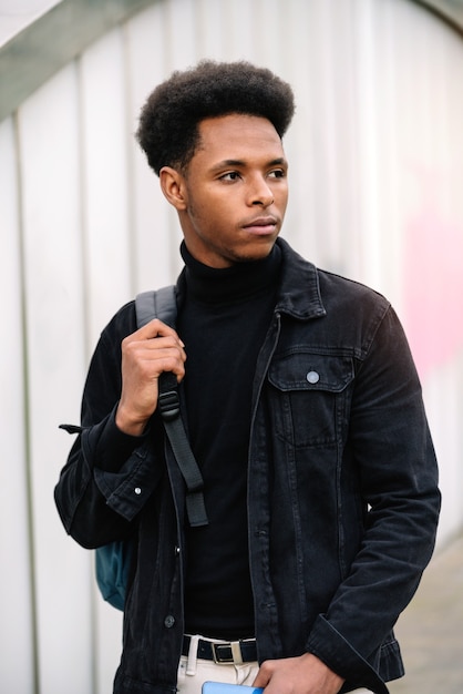 Ritratto alla moda di un bell'uomo marocchino studente con capelli afro in posa e cammina per strada in abiti in stile urbano con una borsa