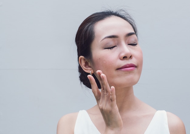 Ritratto asiatico della giovane donna che applica la crema del moisturizer sul suo fronte grazioso.