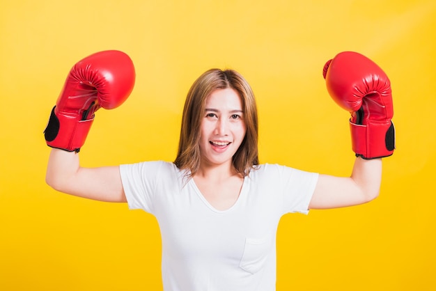 Ritratto asiatico tailandese bella giovane donna in piedi sorriso alzare la mano mostrando le mani durante l'uso di guantoni da boxe rossi, girato in studio isolato su sfondo giallo, c'era spazio per la copia del testo