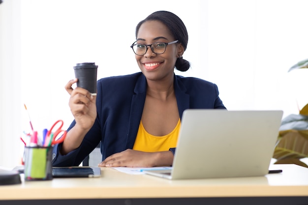 Ritratto Attraente giovane imprenditrice afroamericana che beve caffè nero in un moderno ufficio a casa.