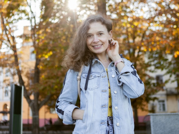 Ritratto autunnale di attraente donna dai capelli ricci in giacca di jeans in città