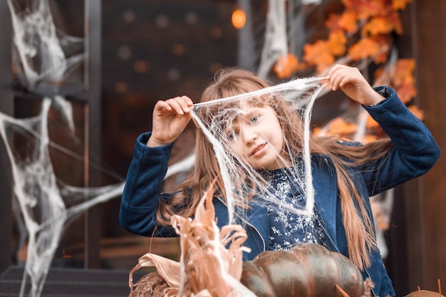 Ritratto autunnale di una bambina che tiene in mano una ragnatela sullo sfondo delle decorazioni di Halloween