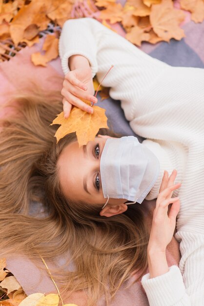 Ritratto autunnale di una giovane donna in maschera medica sullo sfondo di foglie gialle, copia spazio.