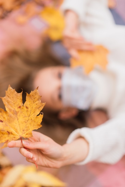 Ritratto autunnale di una giovane donna in maschera medica sullo sfondo di foglie gialle, copia spazio.