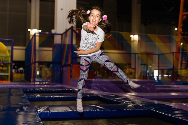 Ritratto bambina carina che gioca e salta sul trampolino nella sala giochi per bambini, parco giochi al coperto. Ragazza attiva che si diverte al centro sportivo.