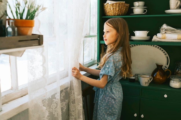 ritratto bambina in abito blu stare vicino alla finestra sulla terrazza primaverile in casa giardino piantine in crescita casa di campagna veranda