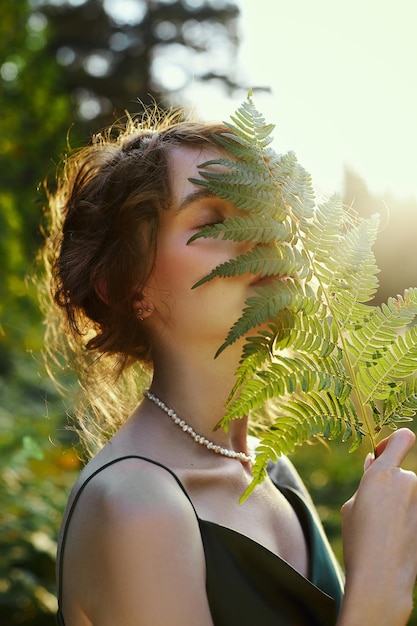 Ritratto bella donna nella foresta al tramonto. La donna sta riposando nella natura, un ritratto d'arte sotto i raggi del sole