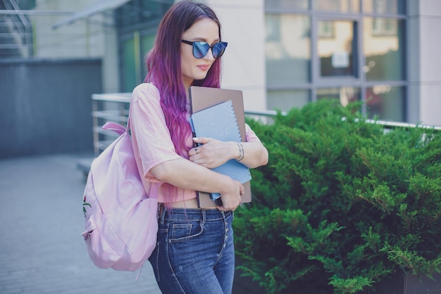 Ritratto bella scrittrice vestita in abito casual che tiene in mano un laptop moderno con uno zaino. Giovane studente di giornalismo di facoltà di buon umore all'aperto