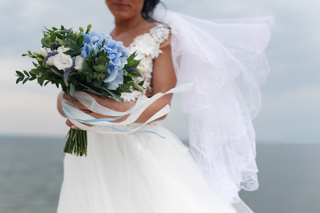 ritratto bella sposa sorridente con un delicato bouquet da sposa nelle mani all'aperto in cielo e sabbia sullo sfondo