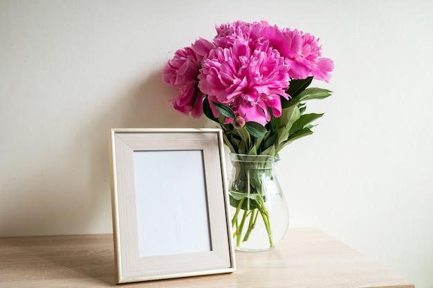 Ritratto bianco cornice mockup su tavola di legno Vaso moderno con peonia Sfondo muro bianco Interni scandinavi