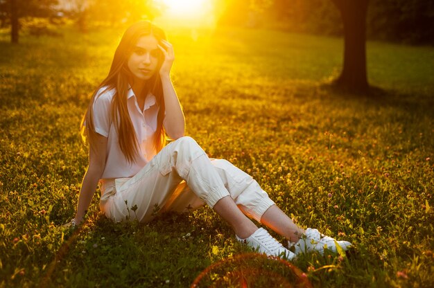 Ritratto caldo della donna sul tramonto che si siede sull'erba