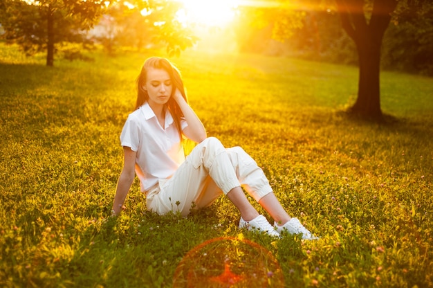 Ritratto caldo della donna sul tramonto che si siede sull'erba