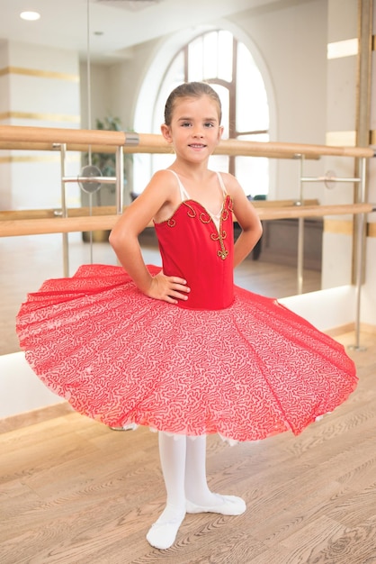 Ritratto carino di una bellissima ballerina in un vestito rosso da spettacolo con tutù rosa Sorride perché è felice di diventare una ballerina professionista in futuro