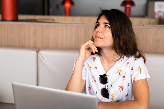 Ritratto casual giovane donna alzando lo sguardo con pensierosa espressione pensierosa Femmina utilizzando il computer