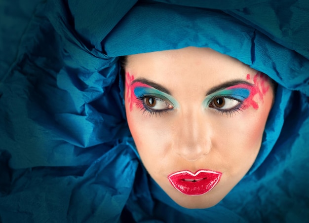 Ritratto d'arte di donna con trucco colorato in turbante blu che guarda l'obbiettivo