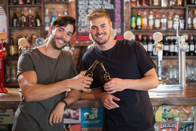 Ritratto degli amici maschii sorridenti che tostano le bottiglie di birra