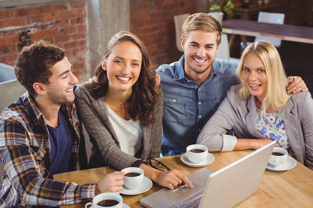 Ritratto degli amici sorridenti che bevono caffè e che utilizzano computer portatile alla caffetteria