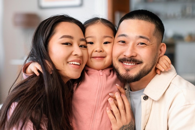 Ritratto dei genitori asiatici felici che abbracciano la piccola figlia a casa