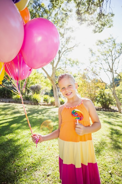 Ritratto dei palloni e del lollypop sorridenti della tenuta della ragazza nel parco