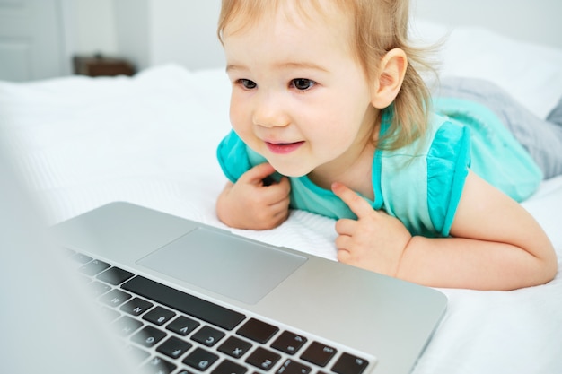 Ritratto del bambino caucasico felice a casa che gioca nel computer portatile