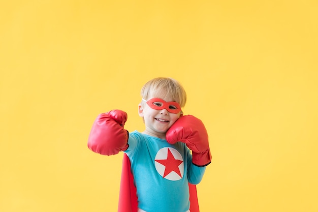 Ritratto del bambino del supereroe. Ragazzo super eroe su sfondo di carta gialla. Bambino felice che indossa maschera rossa e mantello del supereroe. Concetto di sogno e immaginazione dei bambini