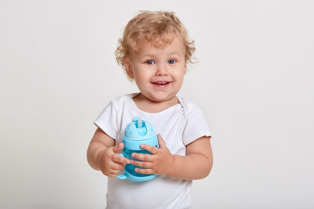 Ritratto del bambino sveglio che tiene la bottiglia d'acqua, bambino che gioca con la tazza blu del bambino