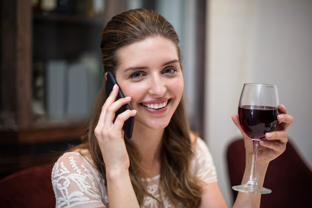 Ritratto del bicchiere di vino della tenuta della donna mentre parlando sul telefono