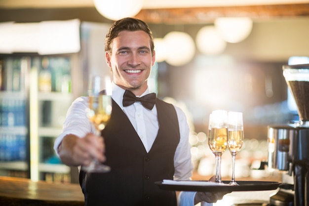 Ritratto del cameriere sorridente che offre un bicchiere di champagne