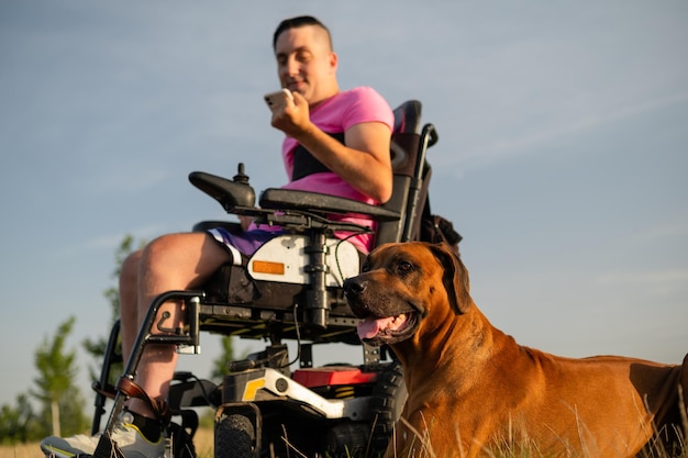 Ritratto del cane guida e di un giovane in sedia a rotelle che usa un telefono cellulare sullo sfondo