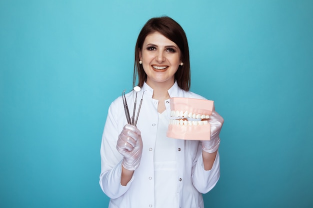 Ritratto del dentista femminile che tiene roba medica e mascella falsa isolata.