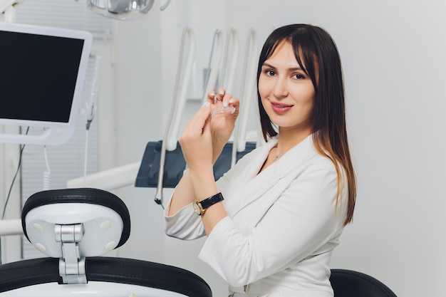 Ritratto del dentista femminile sorridente attraente con le mani piegate.