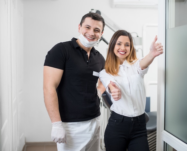 Ritratto del dentista maschio amichevole con il paziente femminile felice dopo il trattamento in studio dentistico moderno.