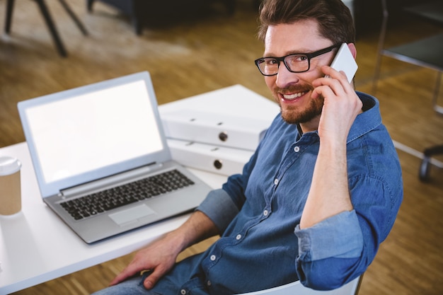 Ritratto del dirigente felice che parla sul cellulare all'ufficio creativo