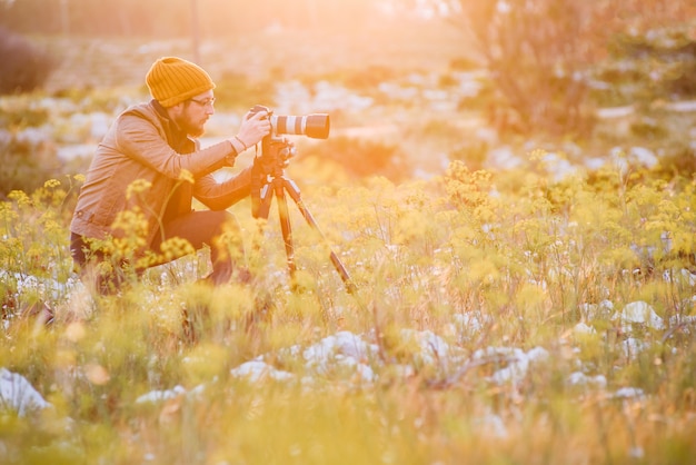 Ritratto del fotografo che fa le foto con la macchina fotografica sul treppiede al tramonto