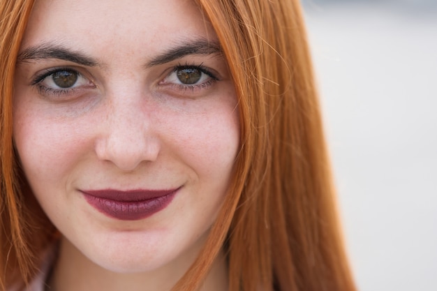 Ritratto del fronte del primo piano di una ragazza con capelli rossi e gli occhi chiari.