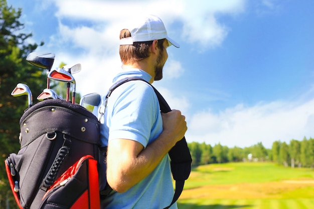 Ritratto del giocatore di golf maschio che trasporta la sacca da golf mentre cammina dall'erba verde del golf club