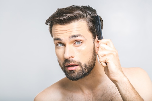 Ritratto del giovane bello che pettina i suoi capelli in bagno. Isolato su sfondo grigio.