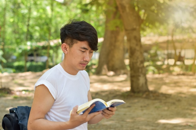 Ritratto del giovane che legge un libro nel parco il giorno di estate.