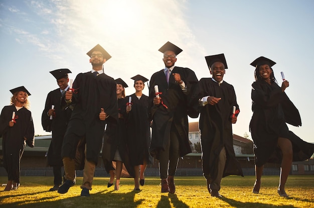 Ritratto del gruppo di laurea e corsa sul prato del campus con il successo universitario celebrazione studentesca e evento di diploma all'università Amici all'aperto e risultati accademici con persone felici e libertà