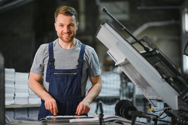 Ritratto del lavoratore della linea di produzione che controlla il processo di produzione della moderna macchina industriale per l'imballaggio nella tipografia