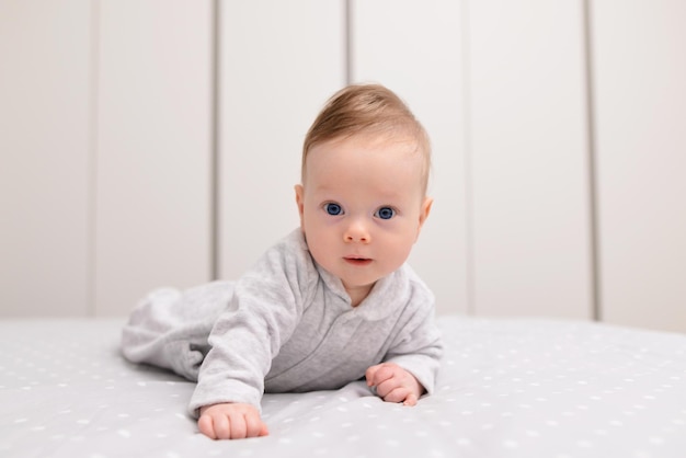 Ritratto del neonato felice sorridente sveglio che striscia sul letto sulla coperta bianca in camera da letto