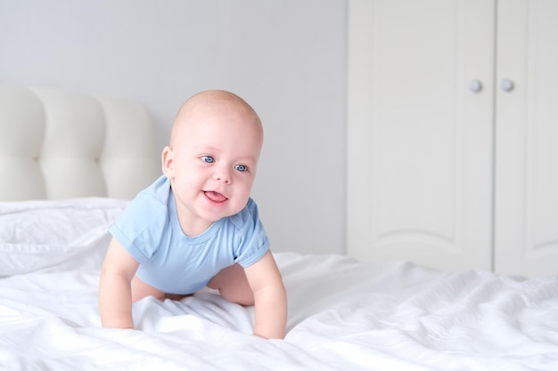 ritratto del neonato sorridente con i grandi occhi azzurri in tuta su biancheria da letto bianca. Neonato sano