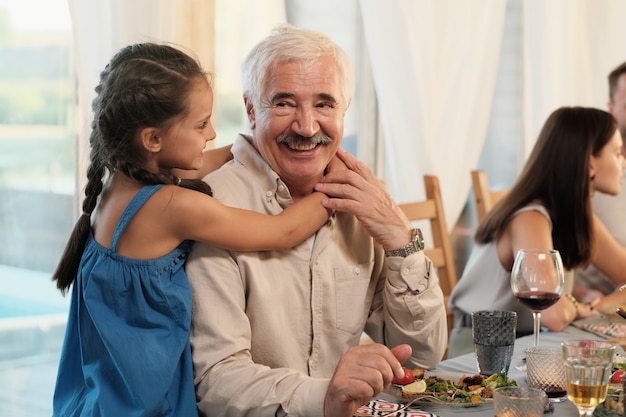 Ritratto del nonno felice che sorride mentre sua nipote lo abbraccia durante la cena a casa