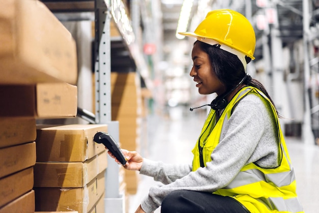 Ritratto del pacchetto di scansione della donna dell'ingegnere afroamericano con lo scanner di codici a barre controlla le merci nel trasporto e nella distribuzione in warehouse.logistic Esportazione industriale e commerciale