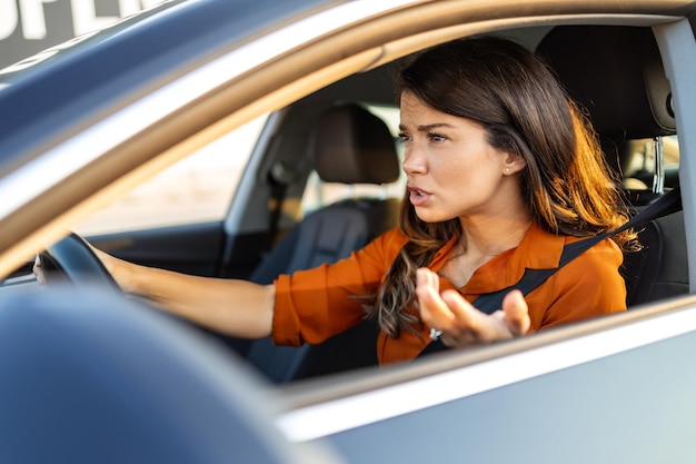 Ritratto del primo piano arrabbiato giovane donna seduta incazzata dai conducenti di fronte a lei Giovane donna seduta in un'auto bloccata in un ingorgo sentendosi stressata perché sta correndo al lavoro