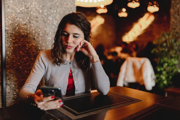 Ritratto del primo piano con la donna abbastanza giovane caucasica che tiene uno smartphone che si siede in un ristorante.